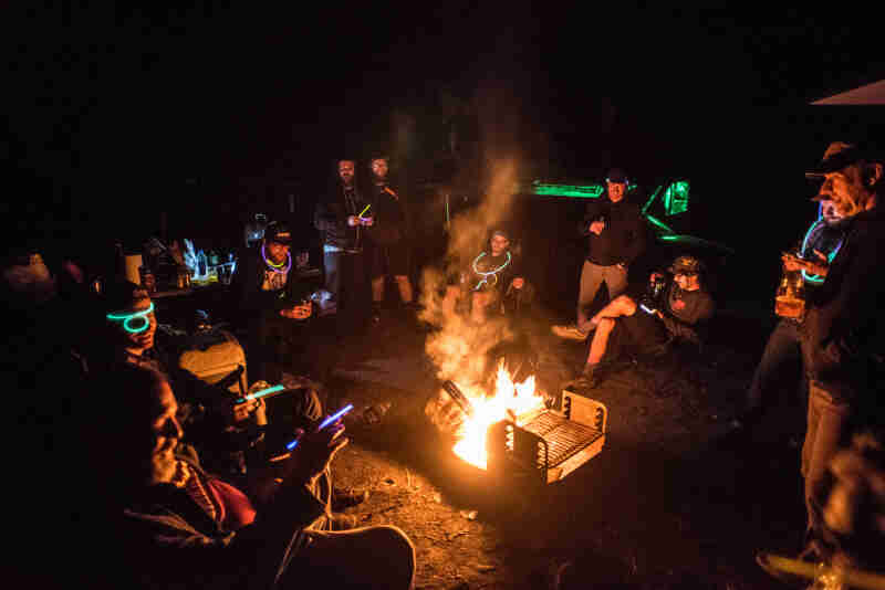 A group of people with glow ropes, sit around a campfire at night