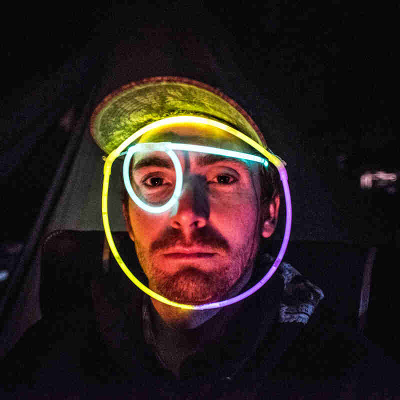 Front view of a person wearing a baseball cap and glow rope around their face, at night