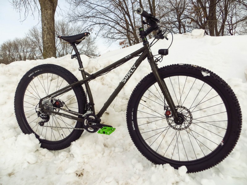 Right side view of a Surly ECR bike, parked across a large snowbank, with bare trees in the background