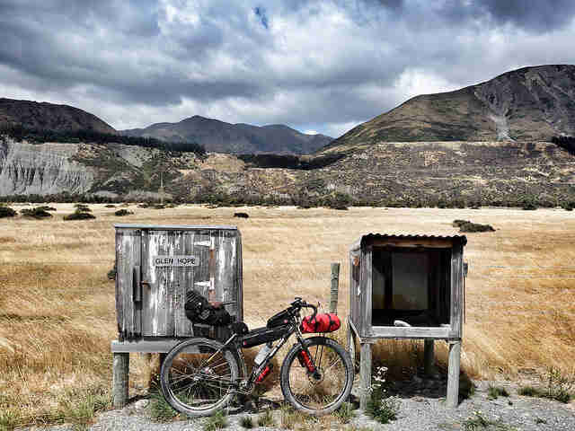 Right side view of a Surly ECR bike, with gear, parked in front of wood boxes, field and mountains in the background