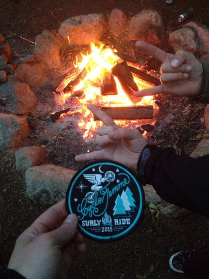 Downward view of 3 hand over a campfire, with one of the hands holding a Cyclofemme Surly Ride 2015 sticker