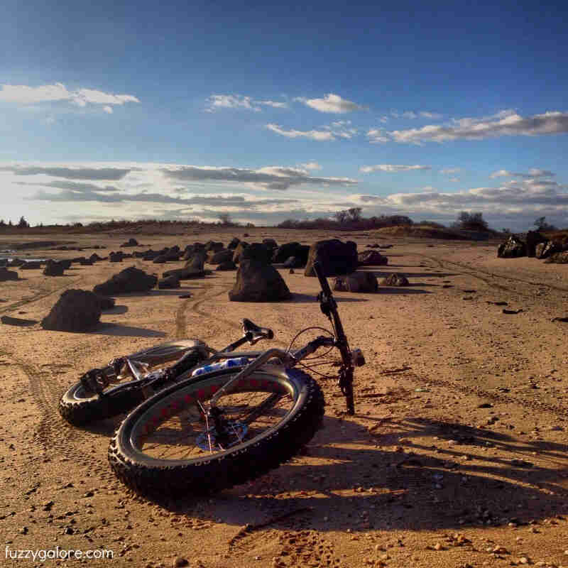 Front, low view of a Surly fat bike, laying on it's left side, in a flat desert field with boulders scattered around