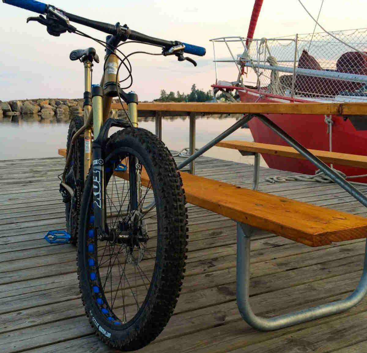 Front view of a gold Surly Instigator bike, leaning against a picnic table on a dock with a boat next to it, in a bay