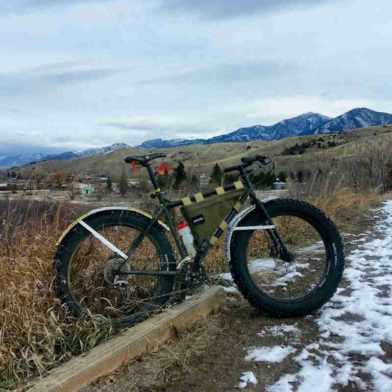 Right side with view of a Surly fat bike, parked on gravel and tall grass, with hills and mountains in the background