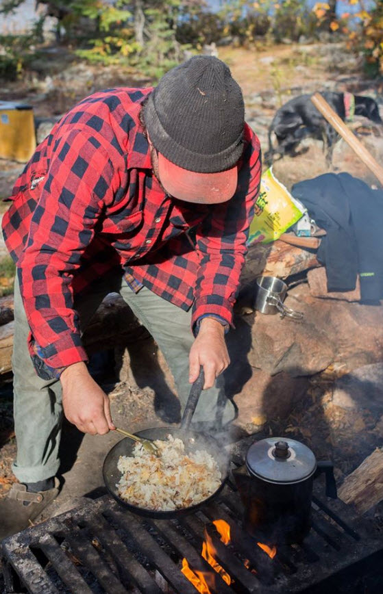 Front view of a person cooking a pan of hash browns over a camp stove