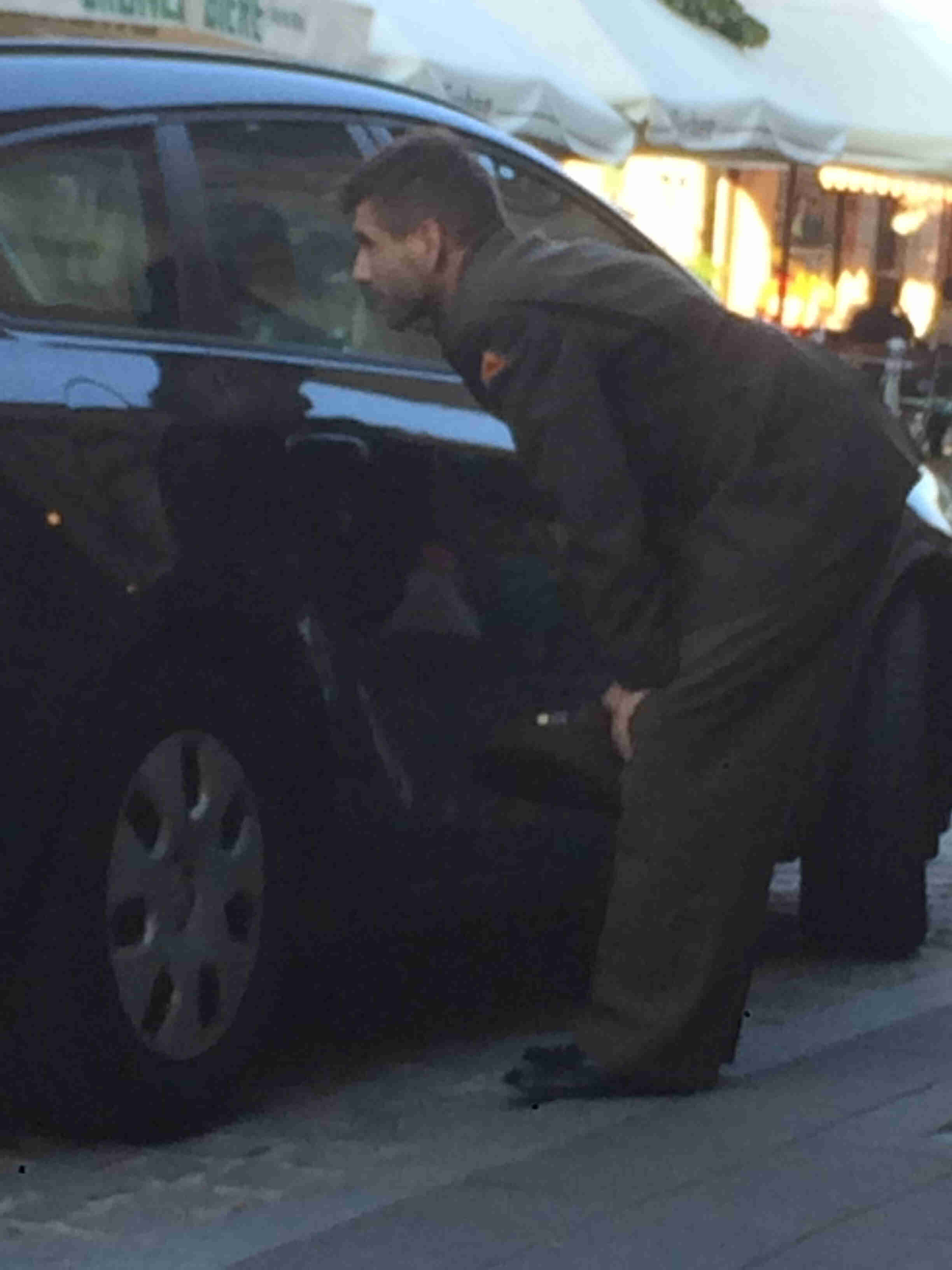 Left side view of a soldier, standing on a sidewalk leaning over, peeking through the rear right window of a black car