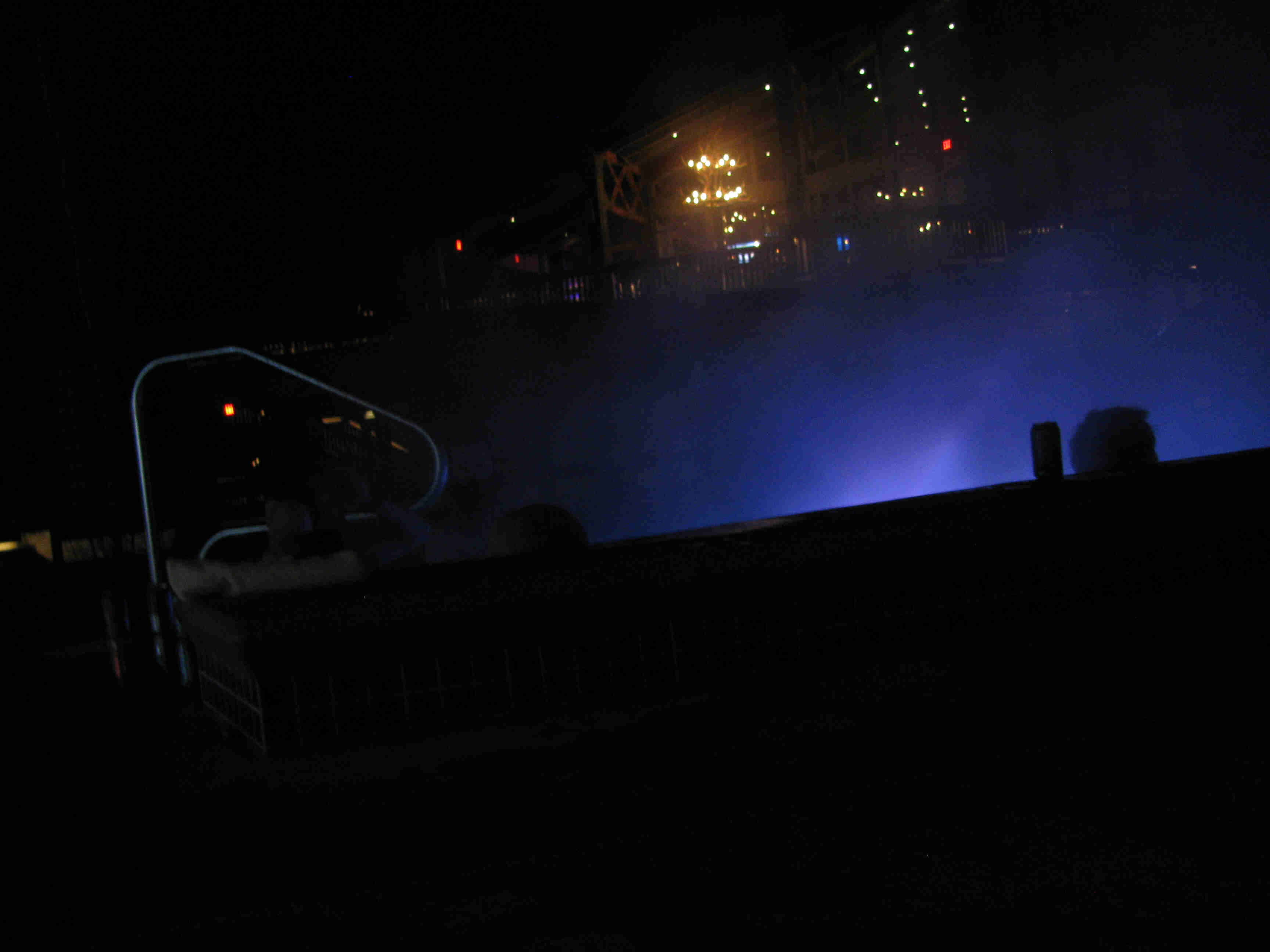 Nighttime view outside of a hot tub with a blue glowing light inside, with lights on a building in the background
