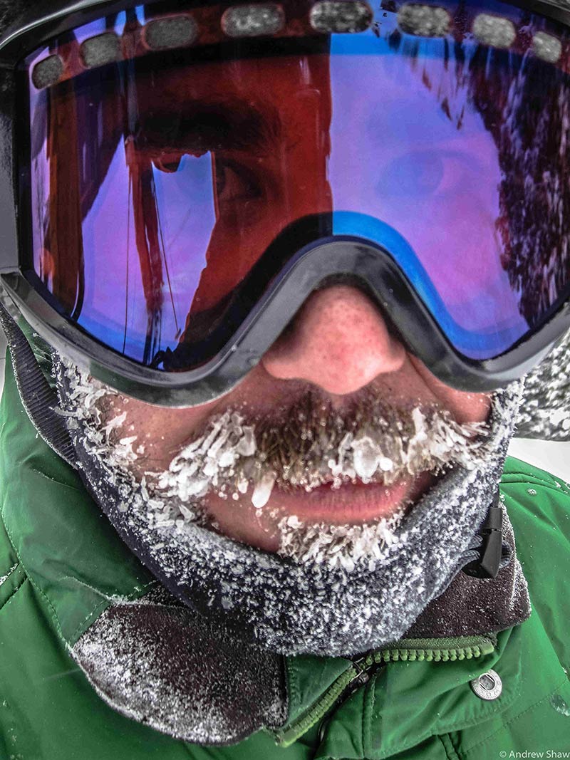 Headshot of a person with ice on the beard and mustache, wearing ski goggles and a green jacket