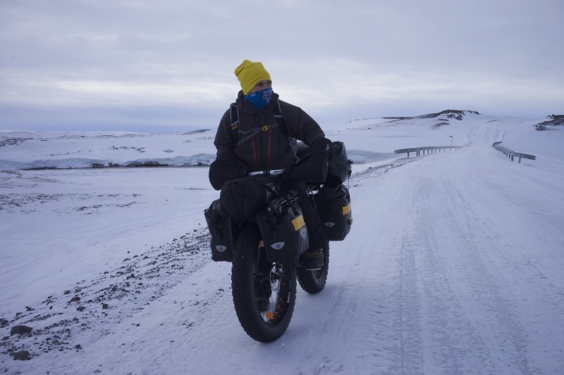 Front view of a cyclist, wearing winter outerwear, riding a Surly fat bike loaded with gear, in a frozen landscape