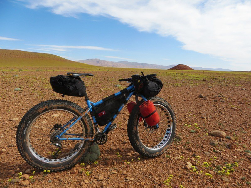 Right side view of a blue Surly Ice Cream Truck fat bike loaded with gear, parked in a rocky desert field