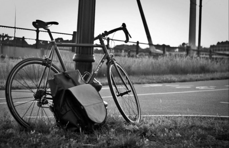 Black & White, right side view of a Surly bike with a pack leaning on the crank, parked along a trail, against a pole