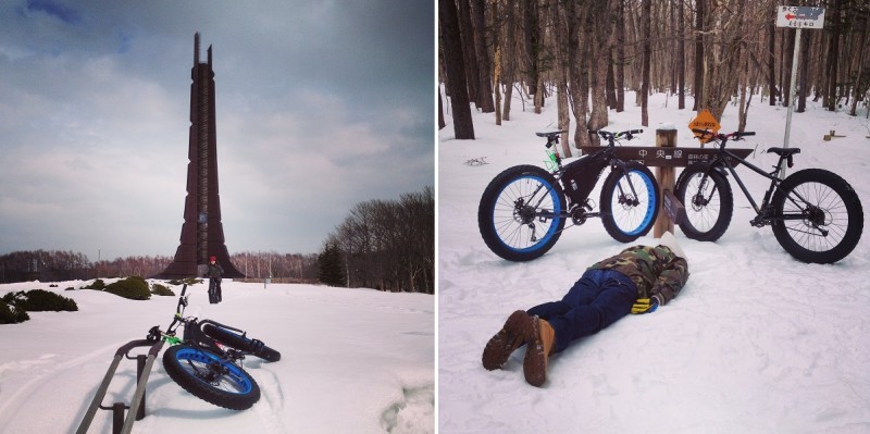 Rear, right side view of a Surly fat bike, laying in a snowy field on a handrail, facing towards a tall sculpture