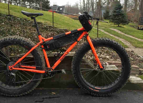 Surly Moonlander fat bike - dayglow orange - right side view - parked on a driveway against a short timber wall