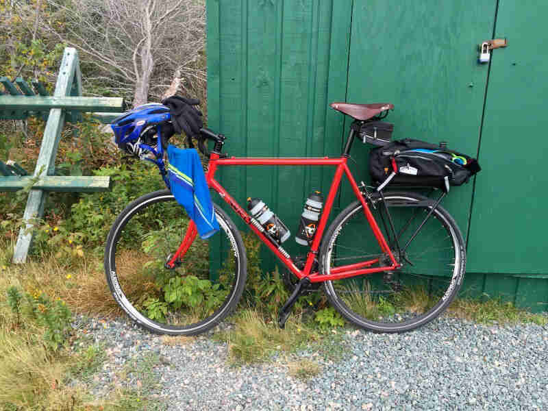 Left side view of a red Surly bike, parked against a green, wood shed