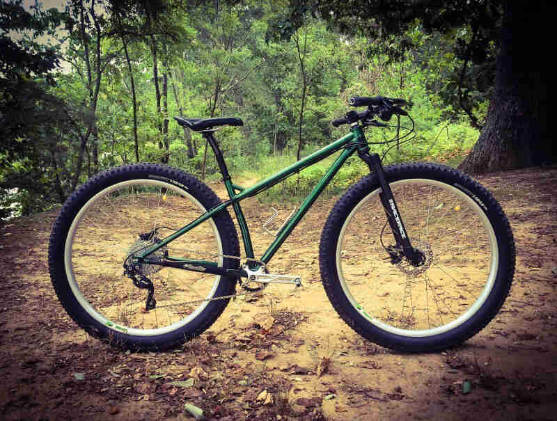 Right side view of an emerald green bike, parked on a dirt lot, with the woods in the background