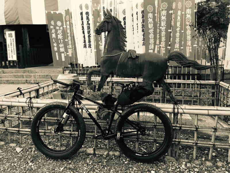 Left side view of black Surly fat bike with gear, parked in front of a bamboo pen with a horse statue inside