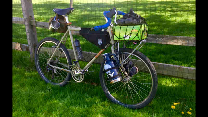 Right side view of a Surly bike, loaded with gear, parked on a grass field against a wire fence
