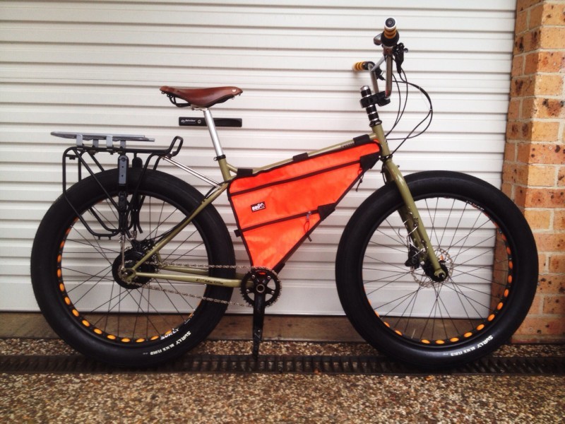 Right side view of a tan Surly Pugsley fat bike with an orange frame back, leaning against the outside of a garage door