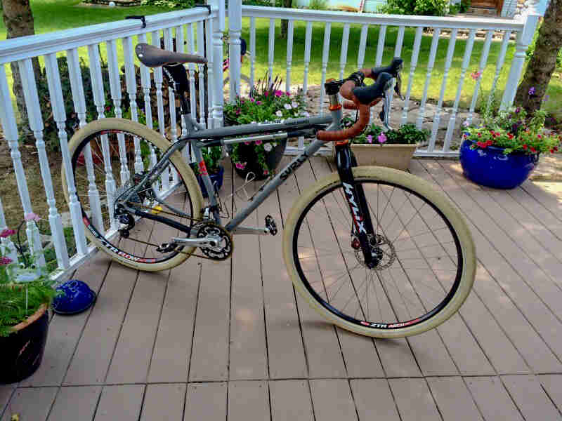 Right side view of a gray Surly Karate Monkey bike, parked on a porch with rear wheel wedged in the handrail balusters