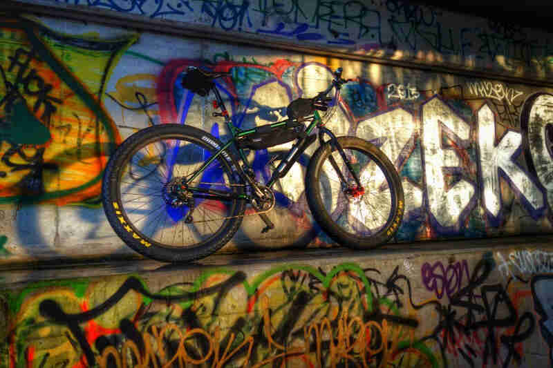 Right side view of a green Surly bike, standing on a cement ledge, leaning on a wall covered in graffiti