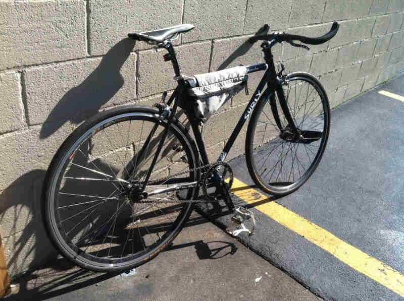 Right side view of a black Surly Steamroller bike, in a parking spot, leaning against a cinder block wall