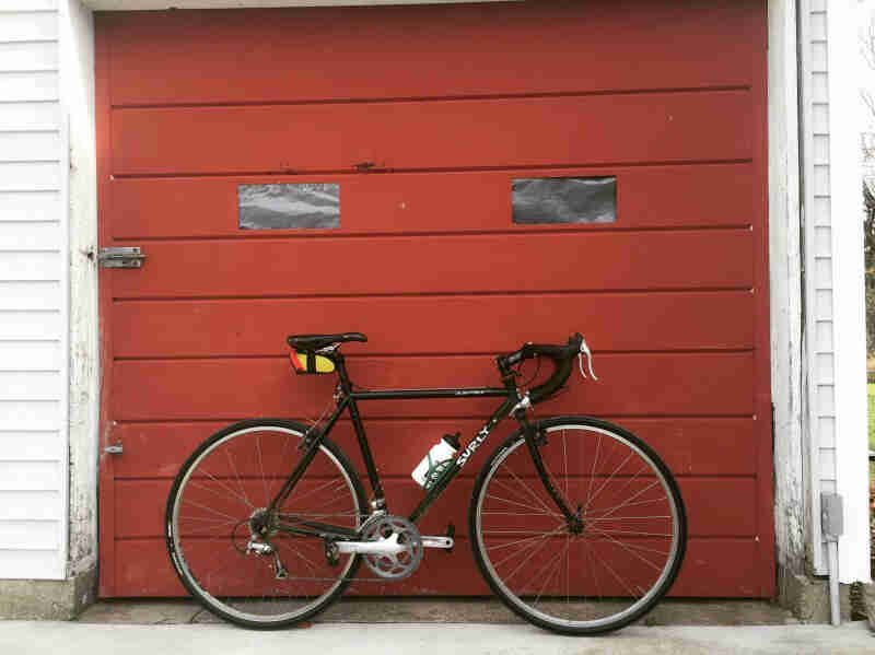 Right side view of a black Surly bike, parked in front of a red garage door