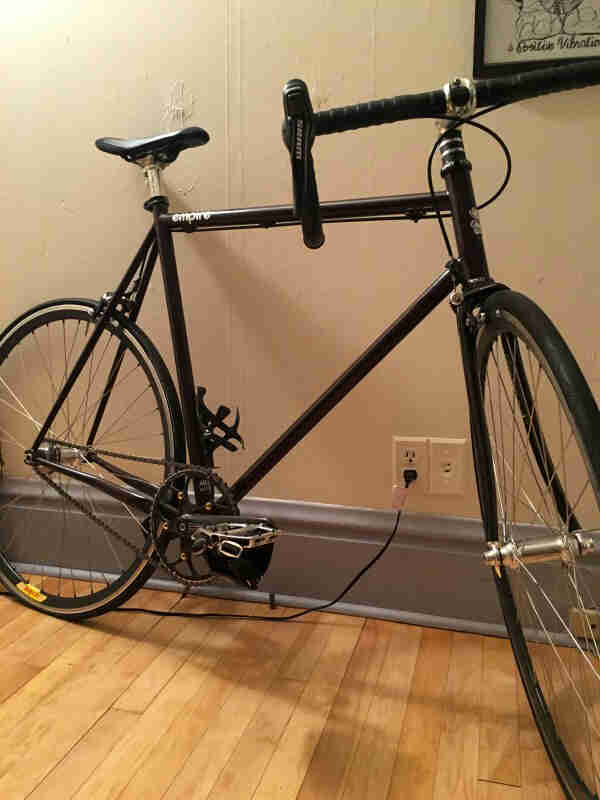 Right view of a black bike on a wood floor, leaning on a wall in a room
