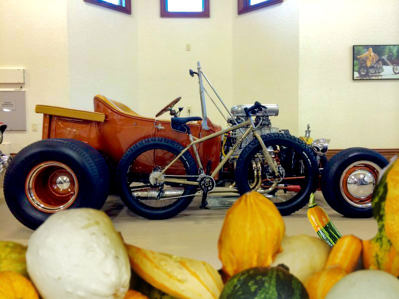 Right profile of a Surly fat bike, tan, parked in front of a rat rod in a garage - gourd graphics below tires