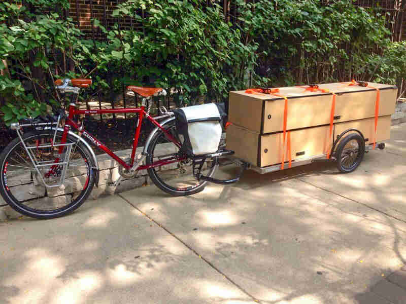 Left side view of a red Surly bike with loaded trailer on back, parked on a sidewalk, in front of a steel fence 