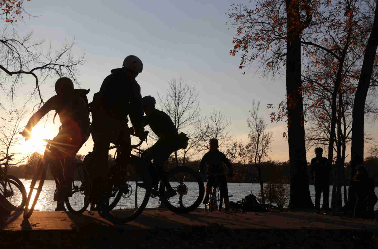 Silhouettes of  three cyclists riding their bikes in a circle, with a lake in the background, at dusk