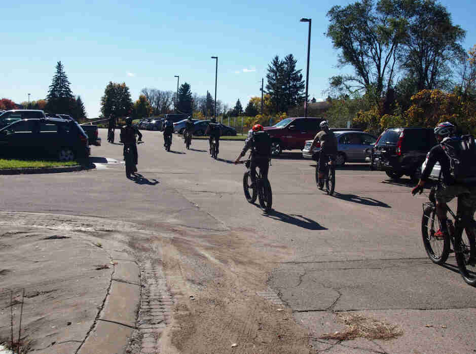 A group of cyclists riding bikes on a paved parking lot
