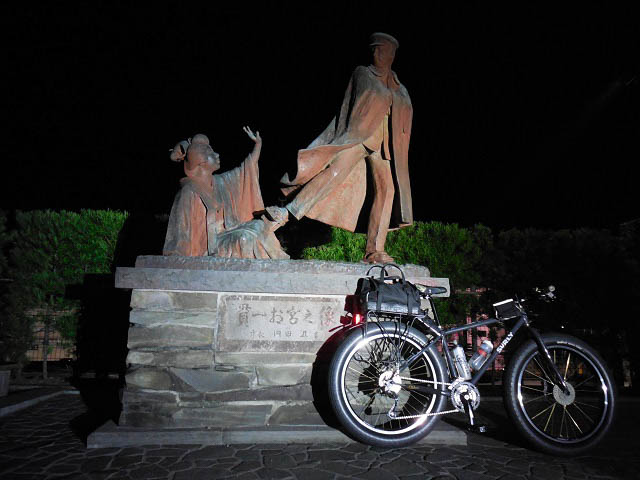 Right side view of a Surly bike, parked against a Japanese statue at nighttime