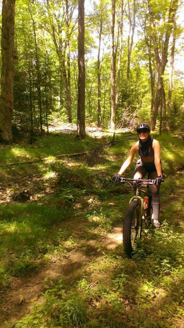 Front view of a cyclist, riding a Surly fat bike, on a grassy dirt trail in the woods