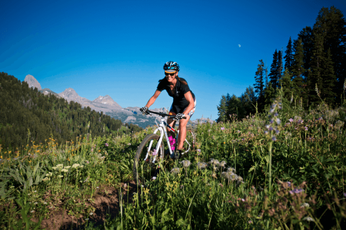Front, right side view of a cyclist on a Surly bike, riding down a hill with thistles, on a dirt trail in the mountains