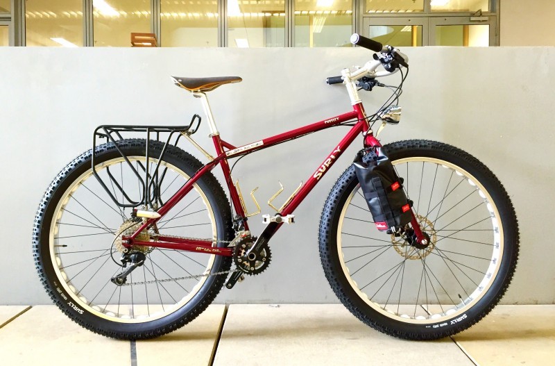 Right side view of a red Surly Pugsley fat bike, parked in front of a wall, with glass building wall in the background