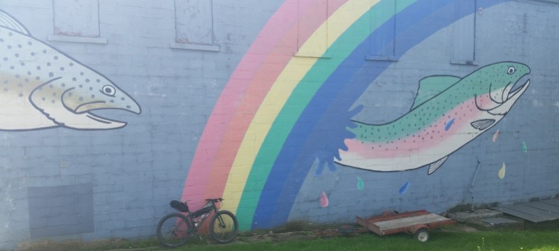Right side view of a Surly Krampus bike with gear, parked against a brick wall with a mural showing trout and a rainbow