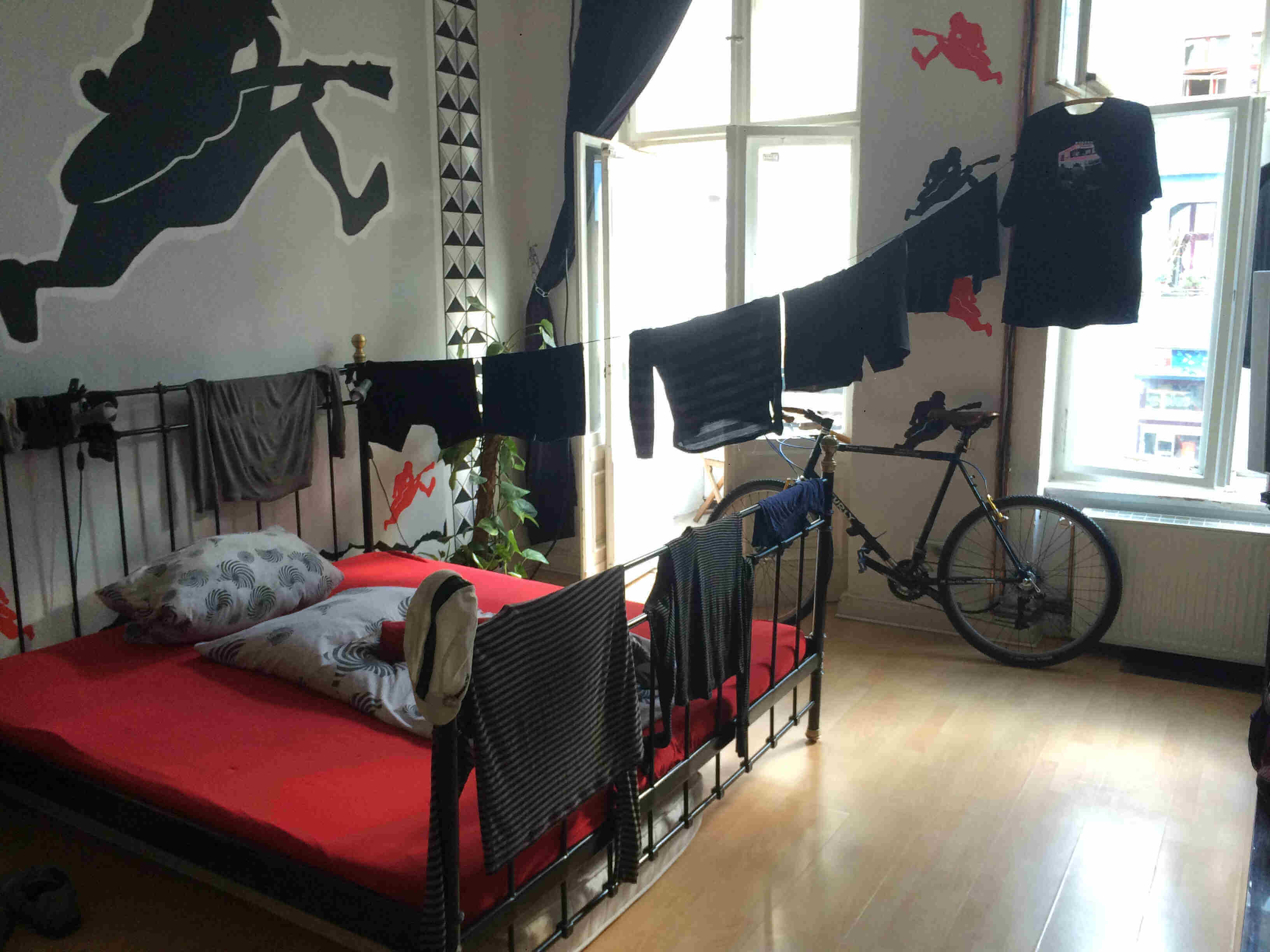 Angled view of a room, with a bed, clothes hanging on a cable, and a black Surly bike leaning next to a glass door