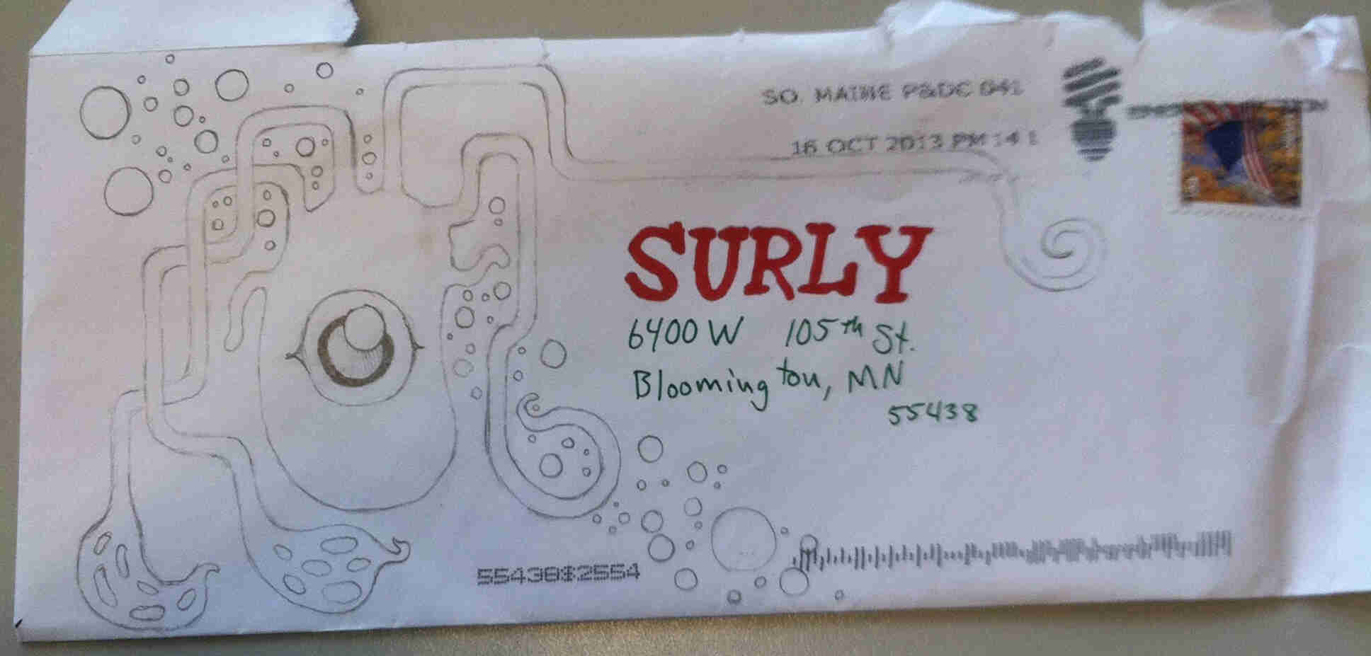 Downward view of a white envelope on a table, addressed to Surly in red marker, with a pen drawing of a squid creature