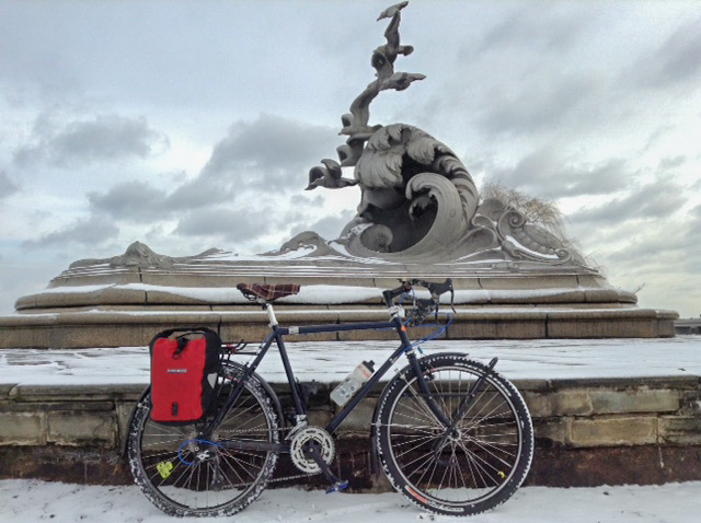 Right profile of a Surly Long Haul Trucker bike, blue, parked on snow in front of a large, frozen, concrete fountain