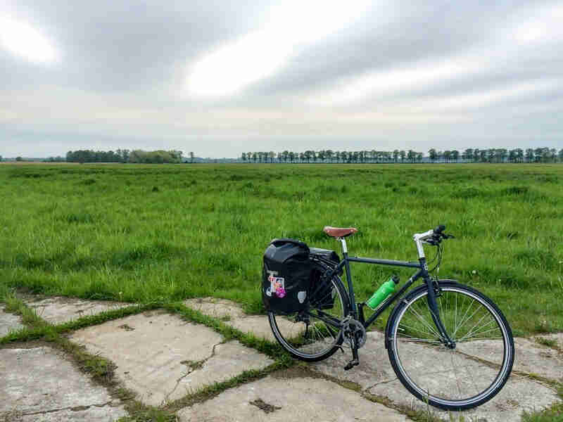 Right side view of a Surly bike with rear saddlebags, parked on large concrete blocks in front of a field of grass