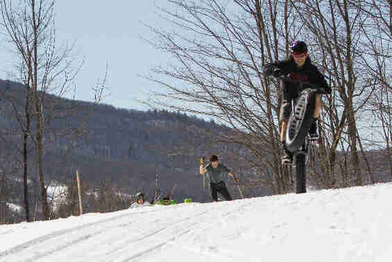 Front view of a cyclist popping a wheel on a snow covered hilltop at a cross country skiing trail