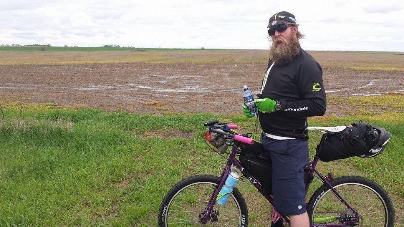 Left side view of a purple Surly bike, with a cyclist standing, staring at the camera, in a grass and mud field