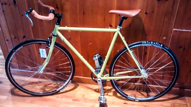 Left side view of a lime green Surly bike, parked against a wood wall