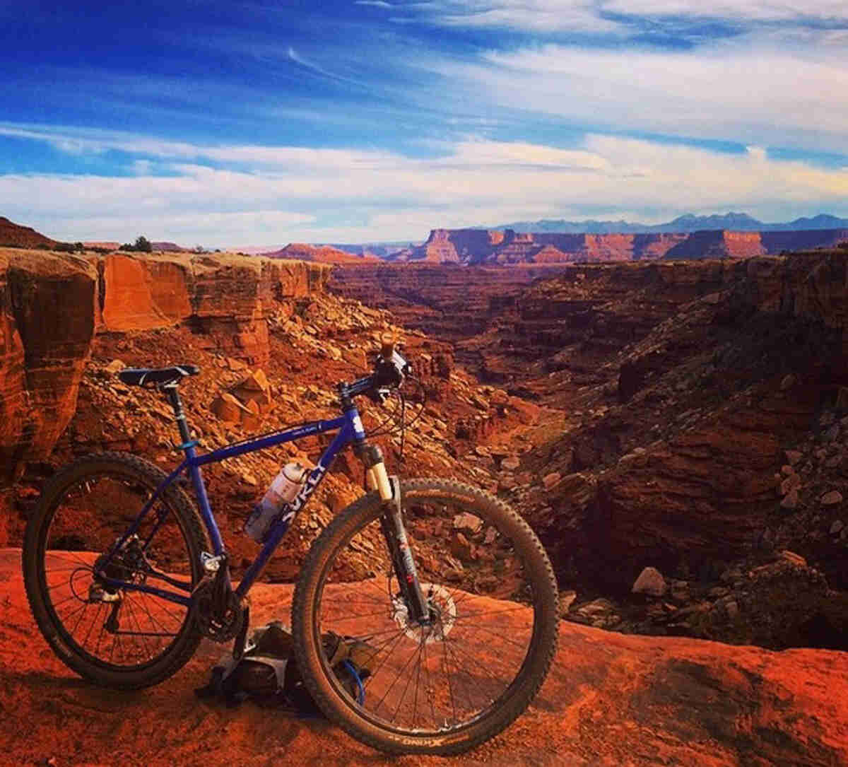 Right side view of a blue Surly Karate Monkey bike, parked on the edge of a red canyon, with buttes in the background