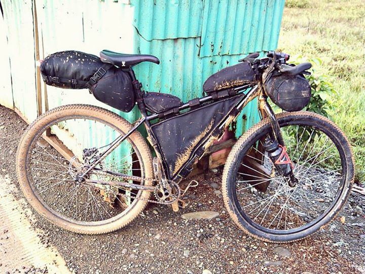Right side view of a black Surly Karate Monkey bike, loaded with gear packs, leaning on a mint, corrugated steel wall