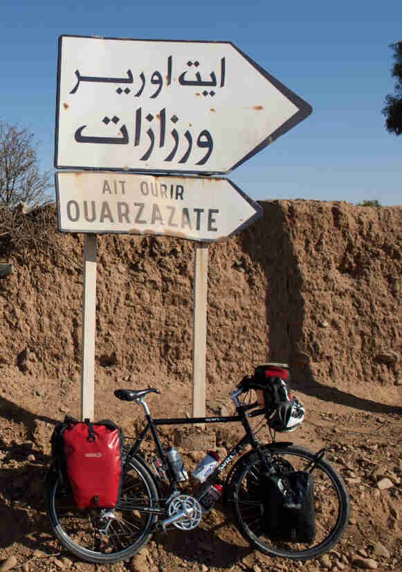 A Surly bike - black - parked against a dirt wall, below a sign