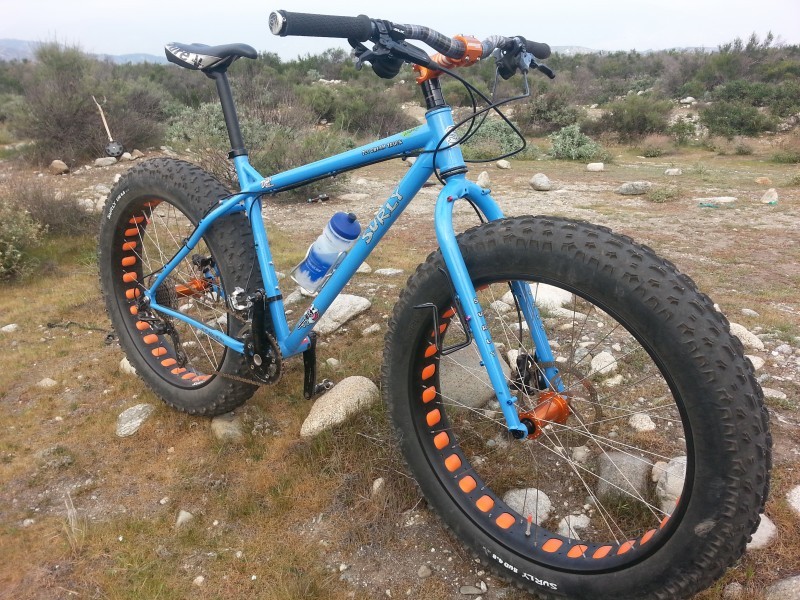 Right side view of a blue Surly Ice Cream Truck bike, parked on a rock and grass clearing of a bushy field