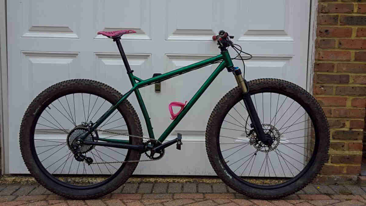 Right side view of a green Surly Krampus bike, parked in front of a white garage door