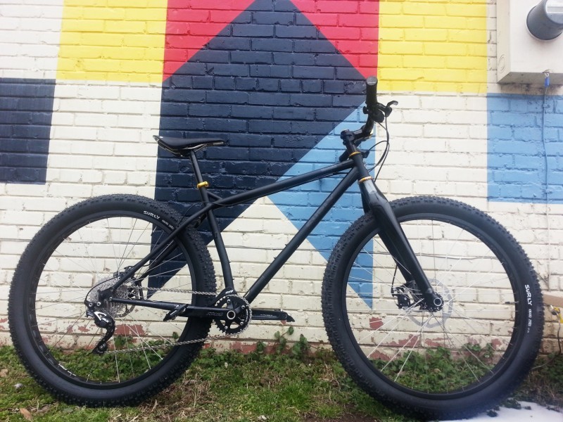 Right side view of a black Surly Krampus bike, parked against a brick wall with painted colored shapes on it