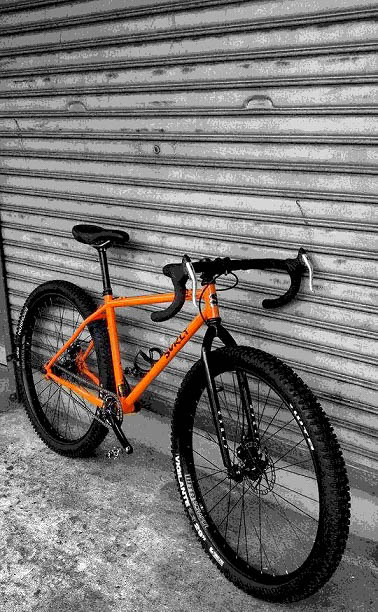 Right side view of an orange Surly bike, parked against a steel garage door